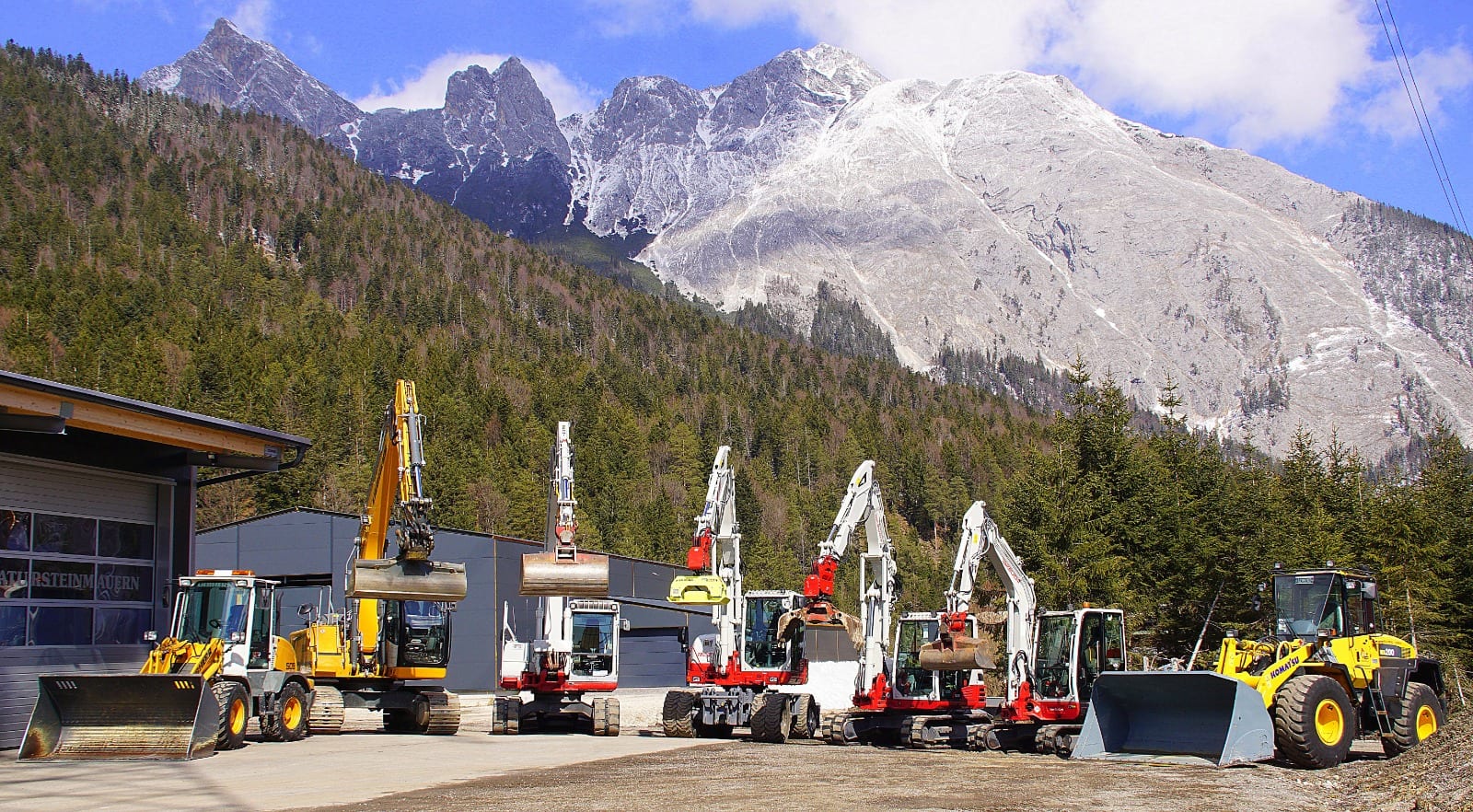 Der Maschinenpark von Erdbau Neuner & Larch mit mehreren Baggern und Radladern vor den verschneiten Gipfeln des Wettersteins.