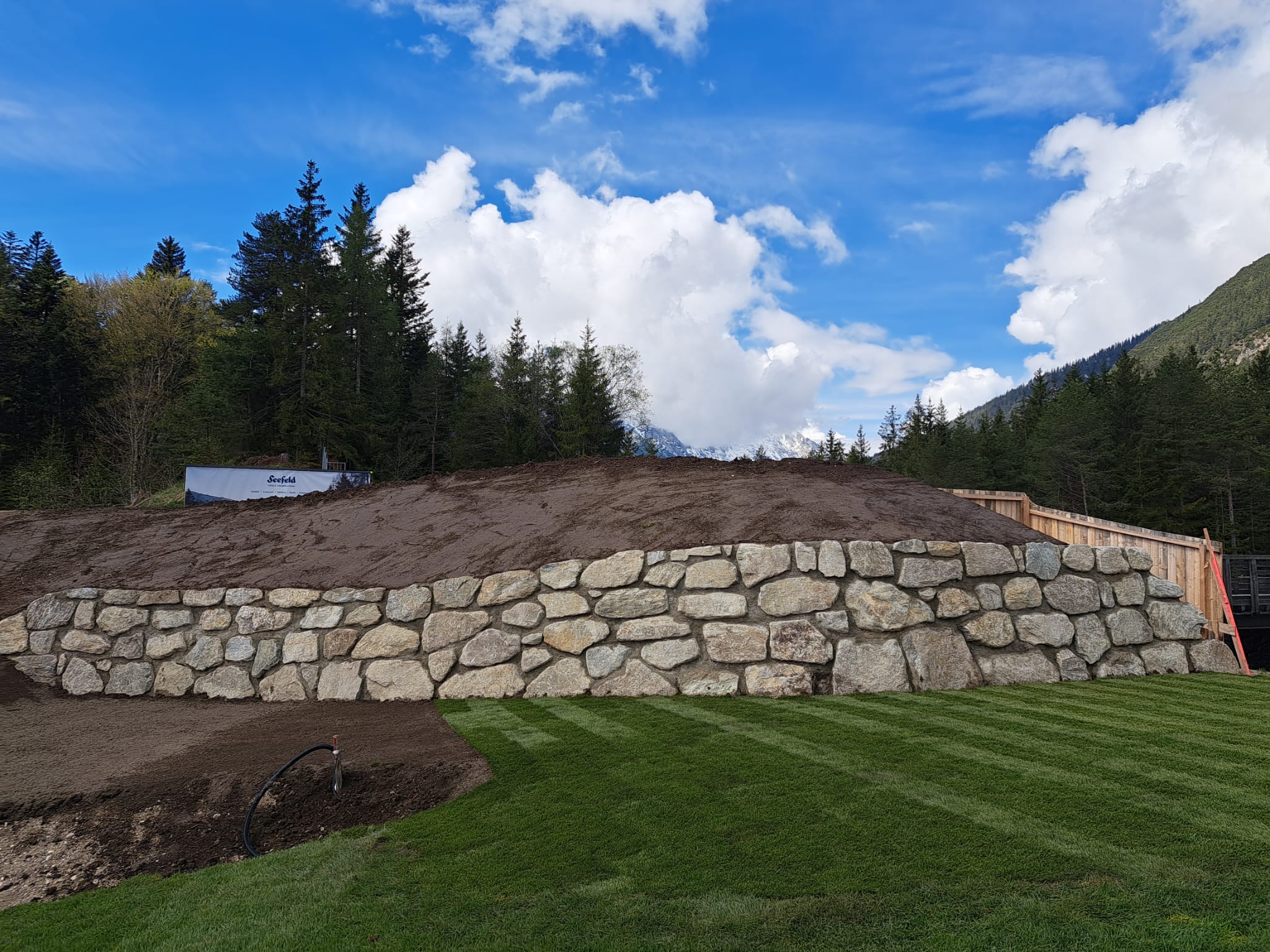 Neu errichtete Natursteinmauer aus Bruchstein mit Rasen davor.