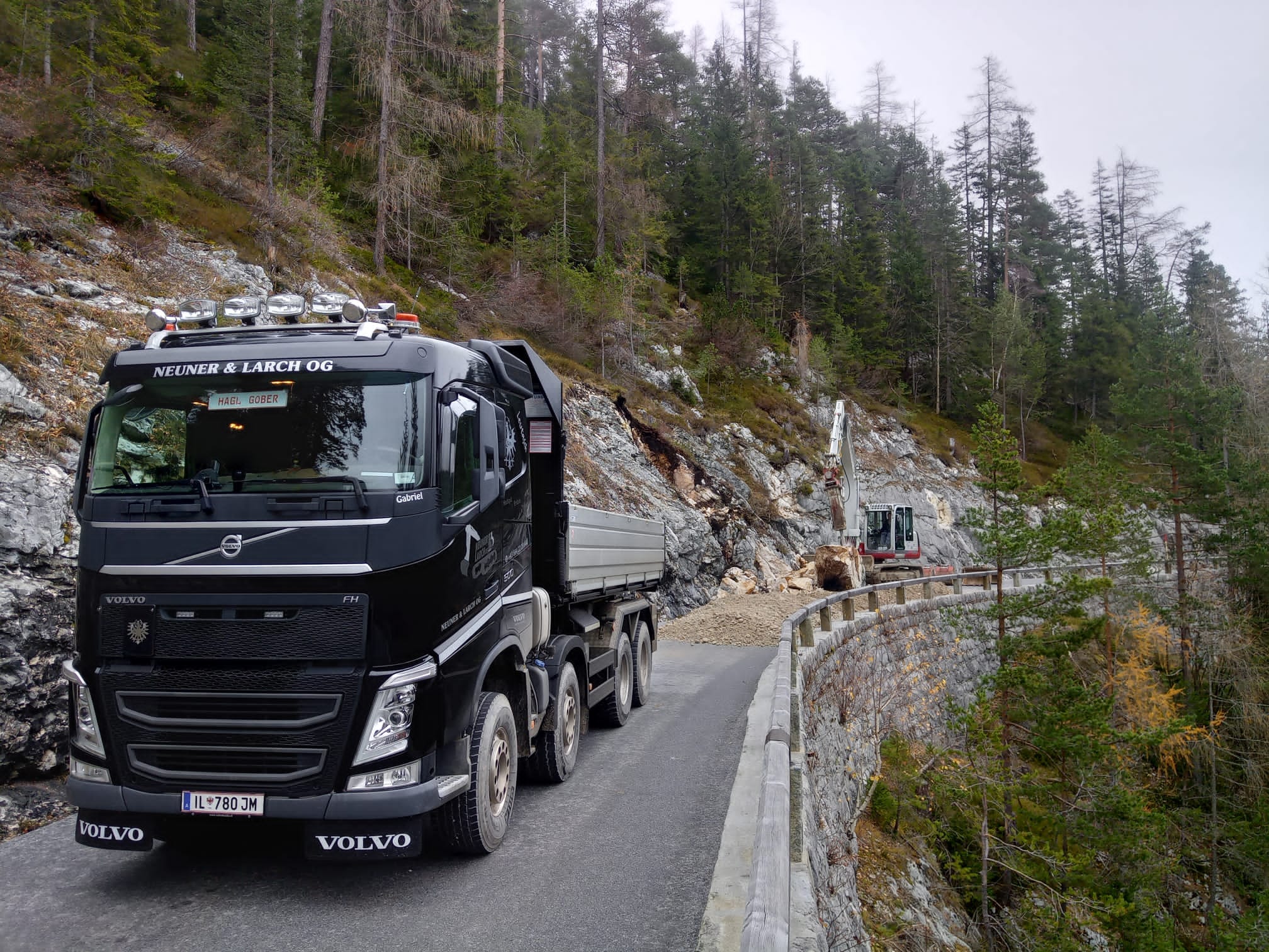 Schwarzer Volvo-Kipper mit der Aufschrift Neuner & Larch OG auf einer schmalen Bergstraße.